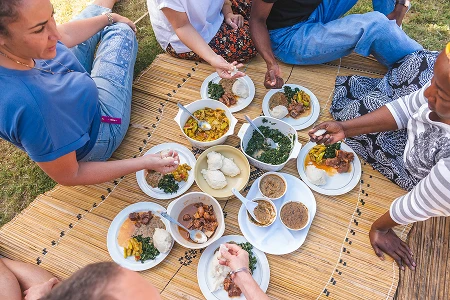 guests sitting on a mat and eating a zambian home cooked meal with their hands
