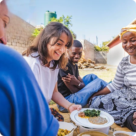 woman sitting outside and serving her plate of food while three people watch