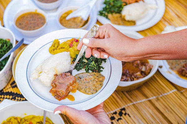 close up of a hand holding a spoon and a plate of home cooked zambian food