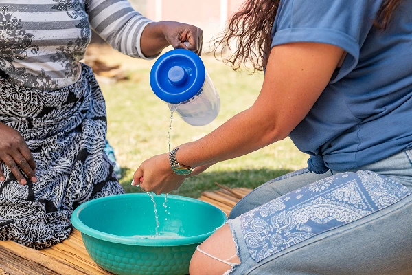 two women washing hands in traditional zambian style with a pitcher and basin