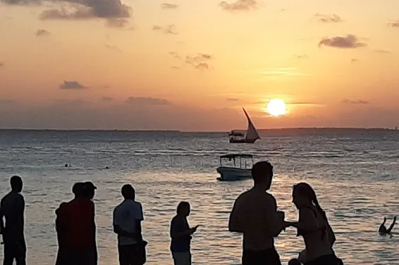 sillouettes of tourists watching sunset at the ocean in nungwi beach