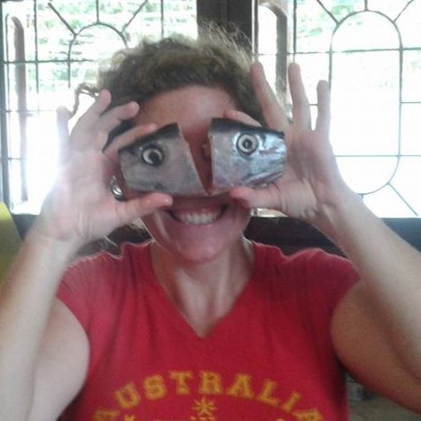 woman in red shirt holding two fish eyes up to her face while laughing