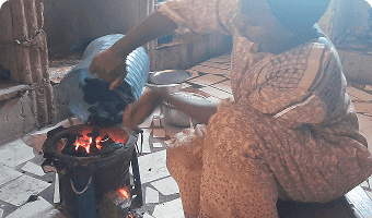 woman pouring container of charcoal onto the fire in her cookstove in zanzibar