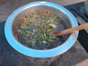 stirring dodo vegetables in a metal pot in rwanda